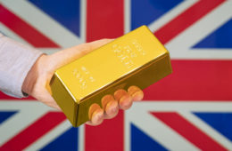 The gold reserve of the Great Britain concept. Gold bar in hand on Britain flag background