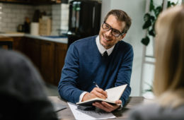 Happy financial advisor communicating with a couple and taking notes into his notebook.