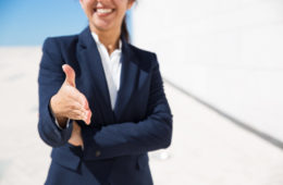 Smiling HR manager congratulating with getting job. Cropped portrait of positive woman in formal suit standing outdoors and offering hand for handshake. Business offer concept